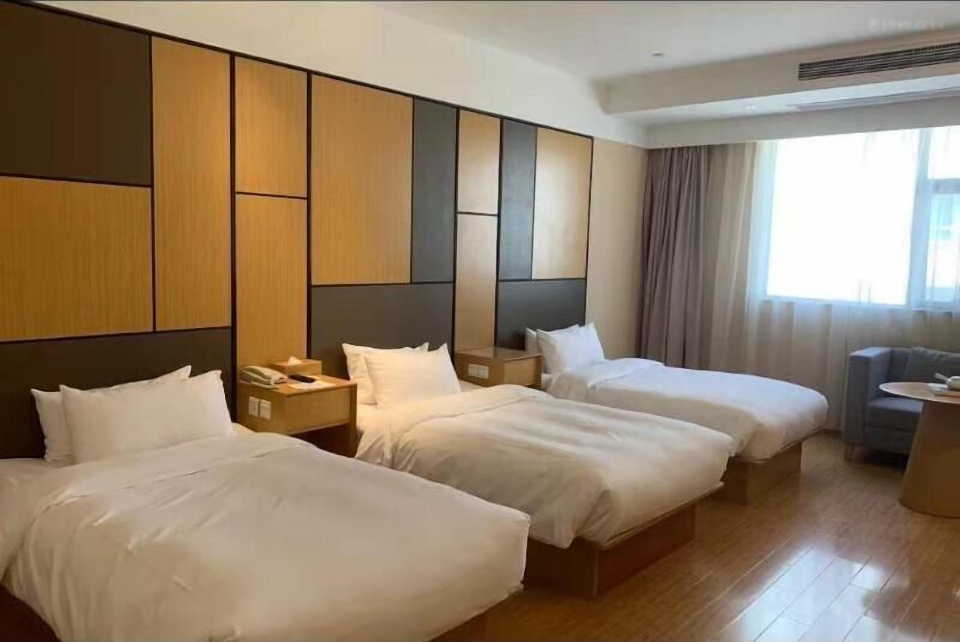 Une chambre d’hôtel avec deux lits simples, un petit bureau, une chaise et une grande fenêtre avec des rideaux.