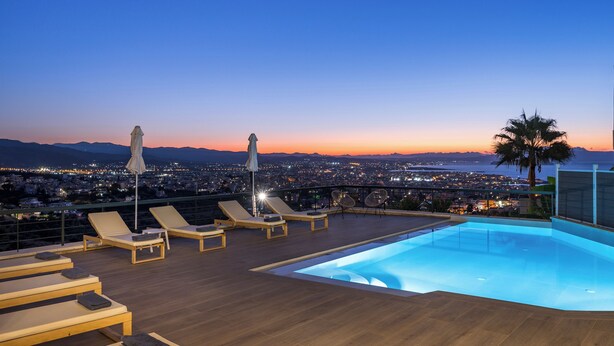 Ein Pool auf dem Dach mit Liegestühlen und Sonnenschirmen, mit Blick auf eine Stadtlandschaft im Abenddämmerung.