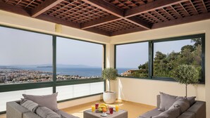 Ein Balkon mit Blick auf Stadt und Meer, möbliert mit einer Couch und einem Tisch mit Früchten und Getränken.