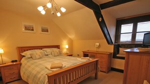 Een slaapkamer met een houten bed, nachtkastjes, een bureau en een televisie.