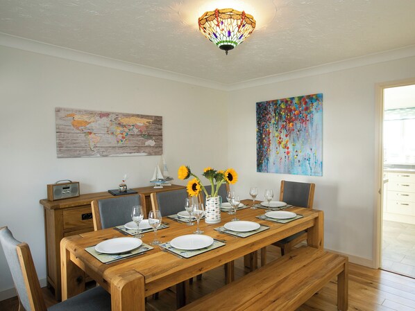 A dining area with a wooden table set for six, a world map, a colorful abstract painting, and a radio on a wooden cabinet.