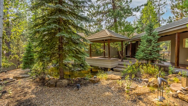 Una cabana amb una zona exterior coberta, envoltada per arbres densos i un petit estany.