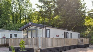 A mobile home with a wooden deck and a fenced patio area. - Tranquil Lodge - UK35277 (Brigham, near Cockermouth)