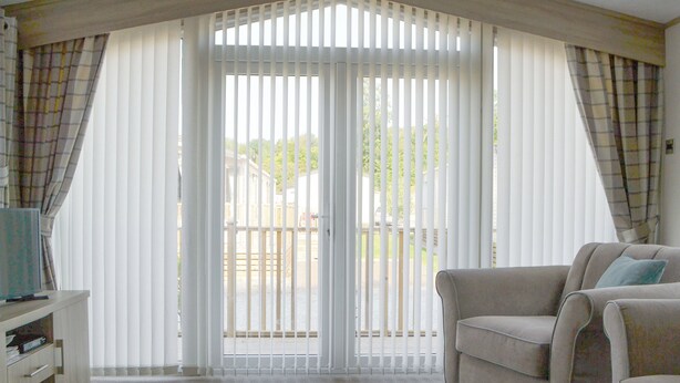A living room with a beige sofa, a coffee table, and a view through a set of white blinds to an outdoor deck. - Tranquil Lodge - UK35277 (Brigham, near Cockermouth)