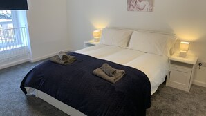 A neatly made bed with a dark blue quilt and two towels, white bedding, and bedside lamps. - Immaculate cosy comfortable home, central location (Inverbervie)