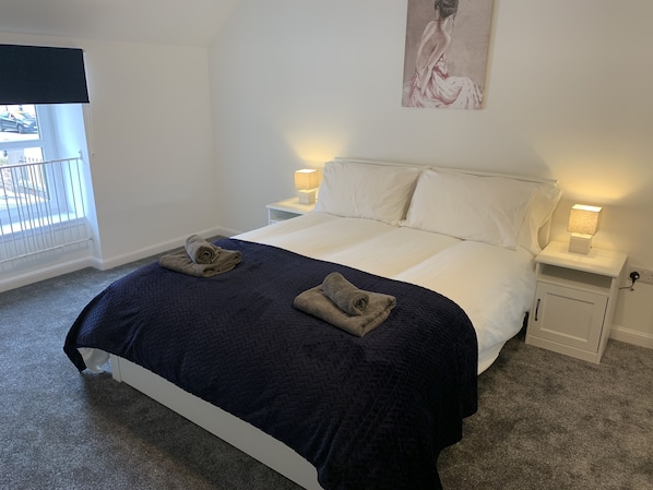 A neatly made bed with a dark blue quilt and two towels, white bedding, and bedside lamps. - Immaculate cosy comfortable home, central location (Inverbervie)