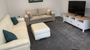 A living room with a beige sofa, a white sofa, and a TV on a wooden stand. - Immaculate cosy comfortable home, central location (Inverbervie)