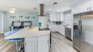 A modern kitchen with white cabinets, a stainless steel refrigerator, and a central island with bar stools. - On the River and oh that view! (Cape Coral)