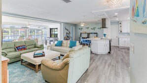 A spacious living area with a green sofa, beige armchair, and a white sofa with blue cushions. A kitchen area is visible with white cabinets and a dining table. - On the River and oh that view! (Cape Coral)