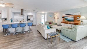 A modern kitchen with white cabinets, a built-in island with blue bar stools, and a dining area with a white sofa and green armchair. - On the River and oh that view! (Cape Coral)