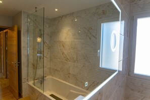 Een moderne badkamer met een glazen douchecabine, een marmeren wand en een groot raam.