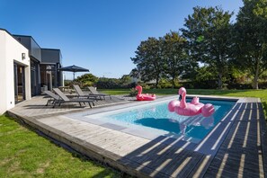 Zwembad met houten terras, ligbedden en opblaasbare flamingo's.