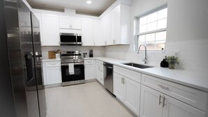 Una cucina moderna con mobili bianchi, elettrodomestici in acciaio inossidabile e una finestra che offre luce naturale.
