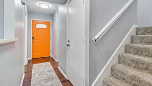 Un pasillo con piso de madera, una puerta blanca con diseño geométrico y una escalera alfombrada.