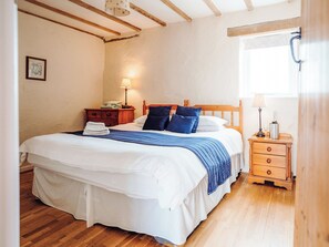 A neatly made bed with a blue blanket, a wooden nightstand with a lamp, and a framed picture on the wall. - The Parlour - UK6717 (Lydstep, near Tenby)