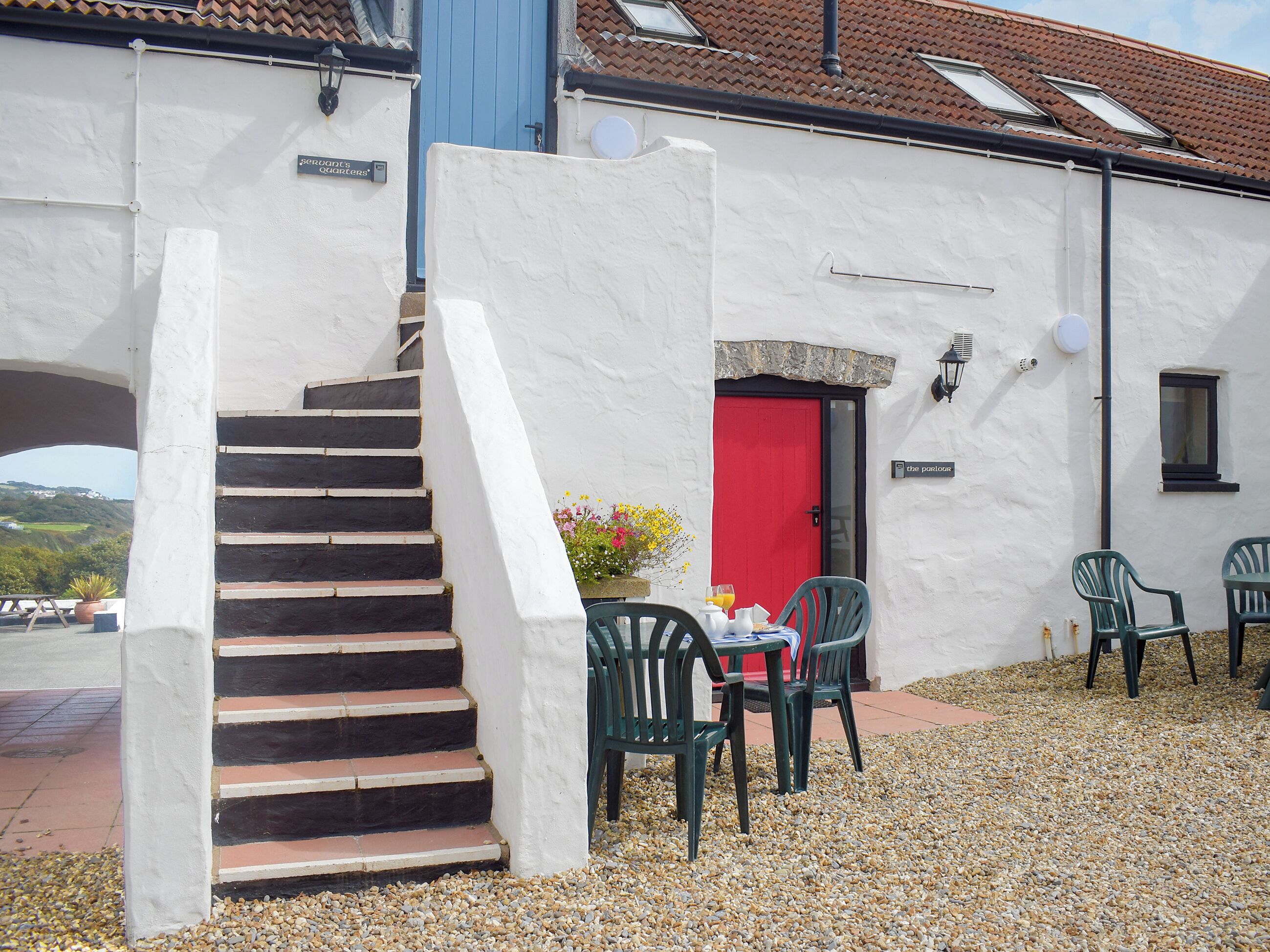 Een gebouw met een rode deur, een trap en terras met stoelen.