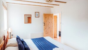 A bedroom with a bed, pillows, a blue blanket, a folded towel, a nightstand with a lamp, a framed picture, and a wooden door. - The Parlour - UK6717 (Lydstep, near Tenby)