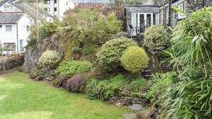 Un bâtiment en pierre avec un jardin, une maison blanche et un petit étang.
