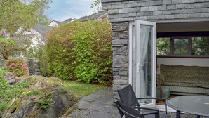 Une maison en pierre avec une porte en verre donnant sur un patio aménagé avec une table et des chaises.