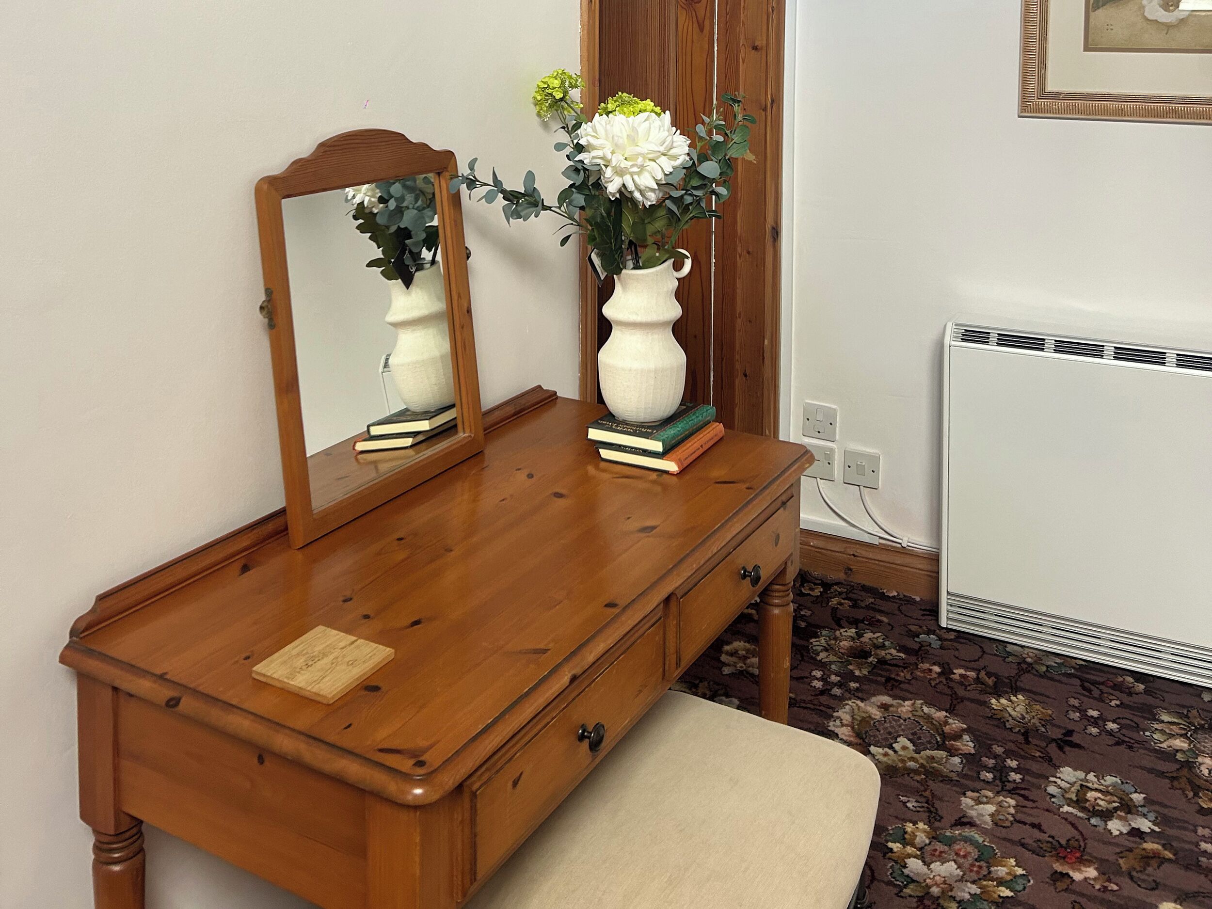 Un aparador de madera con un espejo, un florero con flores y libros.