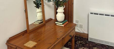 Un aparador de madera con un espejo, un florero con flores y libros.