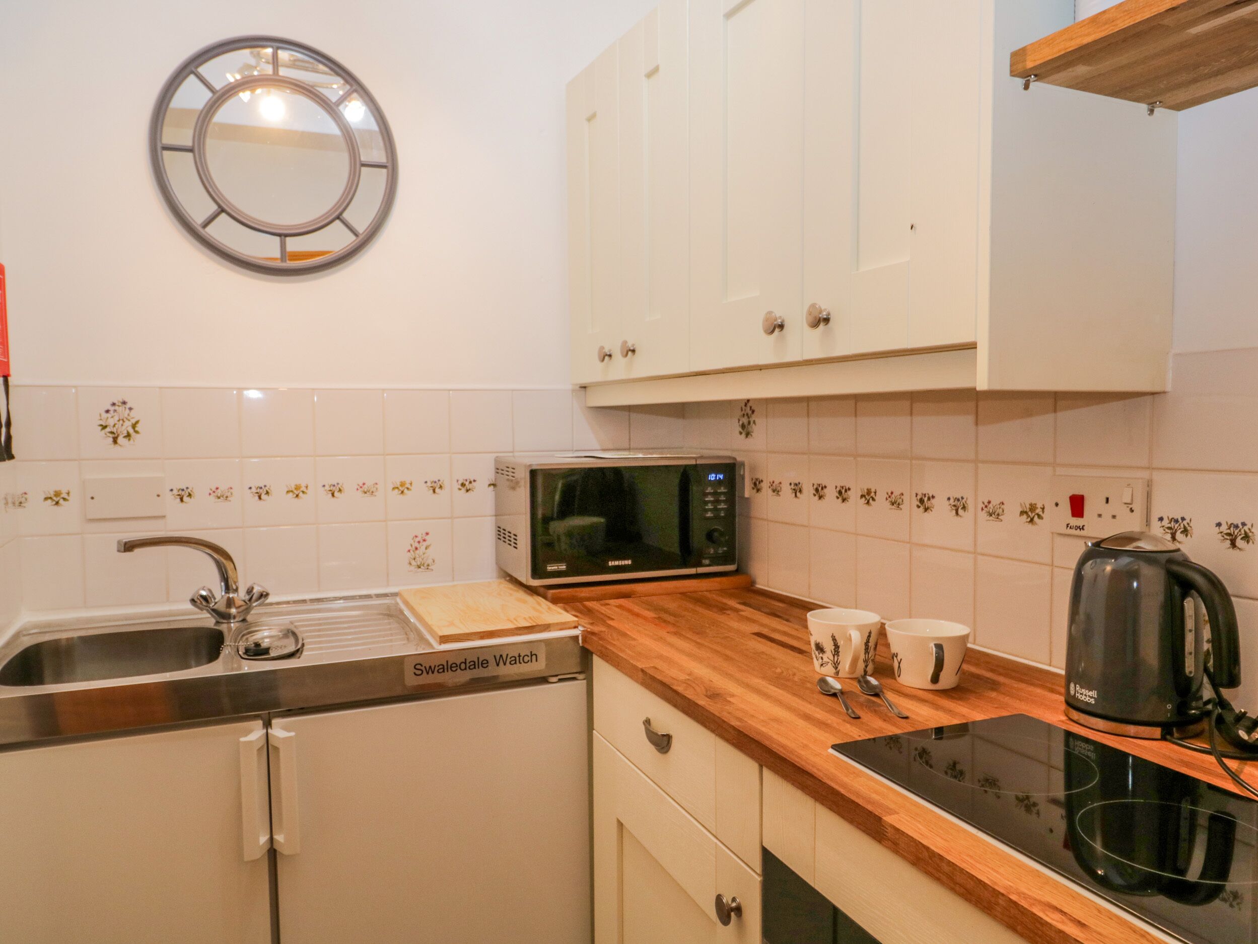 A kitchen with white cabinets, a microwave, a kettle, and a sink.