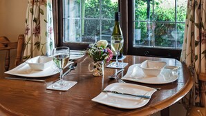 A dining table set for four with plates, cutlery, and glasses, a bottle of wine, and a vase with flowers. - Toms Cabin - UK35173 (Stelling Minnis, near Canterbury)