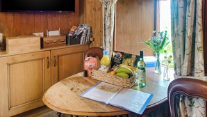 A wooden interior with a round table, a television mounted on the wall, and a window with curtains. - Mains of Auchmedden Cottage (Near Pennan)