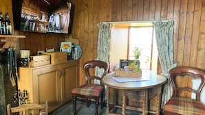 A wooden cabin interior with a wooden table, two chairs, a fireplace, and a television mounted on the wall. - Mains of Auchmedden Cottage (Near Pennan)