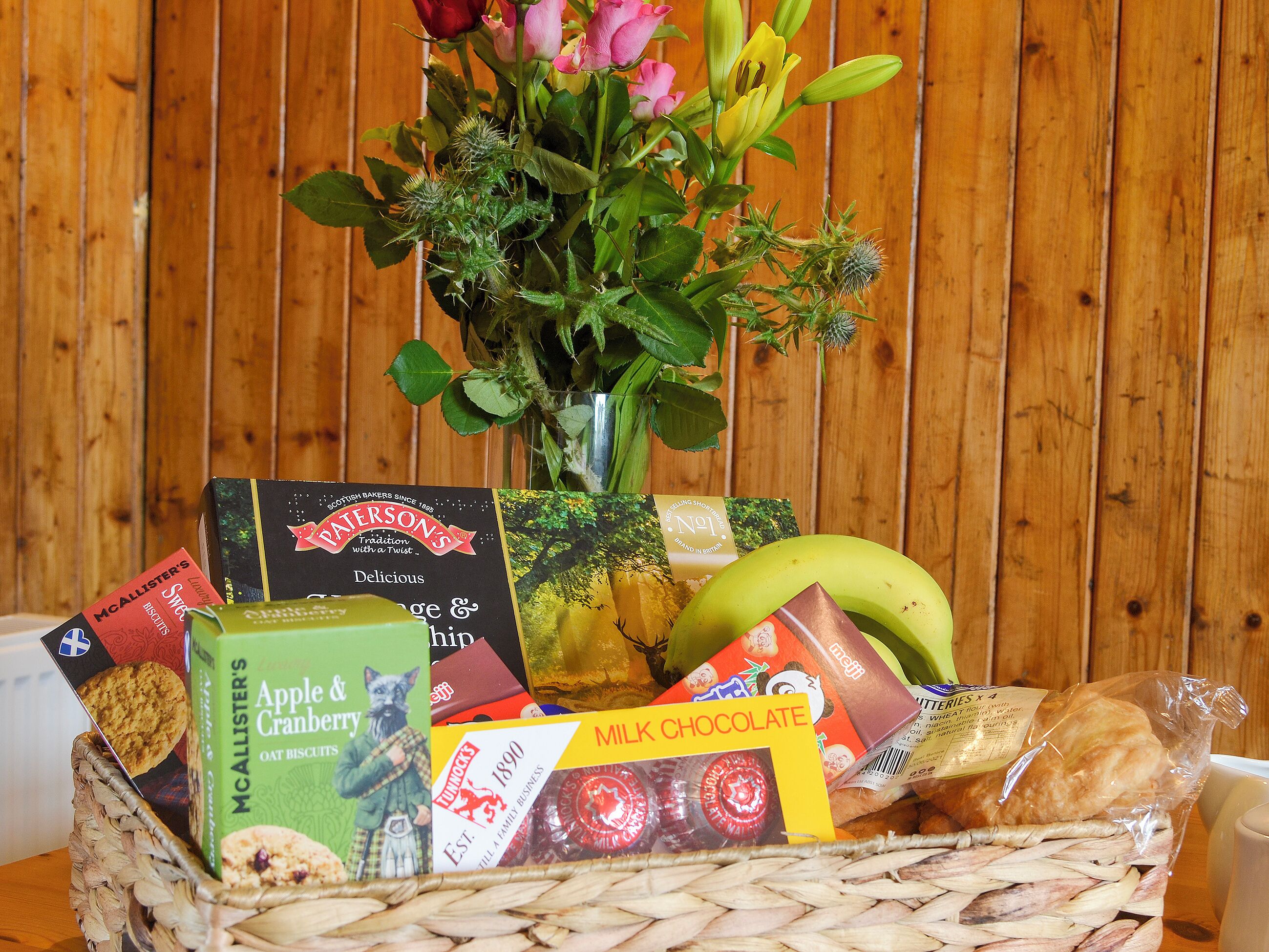Un panier en osier rempli de divers aliments et un bouquet de fleurs.