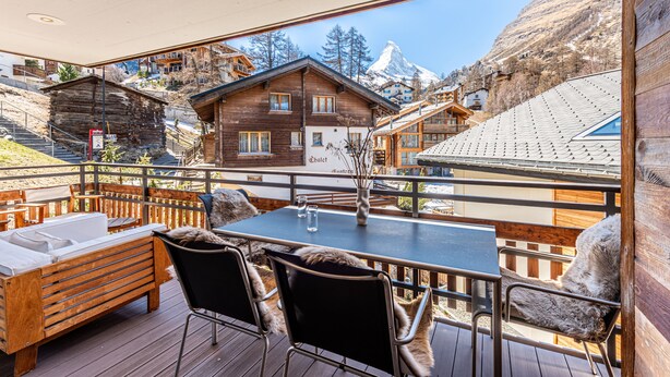 A wooden deck with a table and chairs, a sofa, and a view of a mountain. - Luxurious Chalet Petit - matterhorn views, central location, outdoor hot tub (Zermatt)