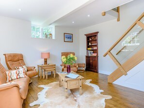 A living room with a sofa, a coffee table, a chair, a lamp, a bookshelf, and a staircase.