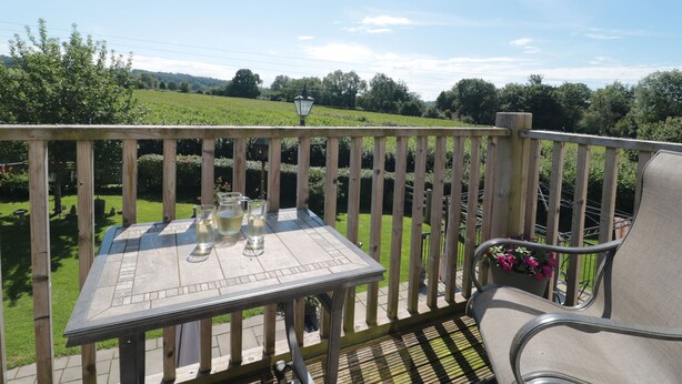 A wooden deck with a table and chairs, overlooking a green field. - The Cider Shed (Winscombe)