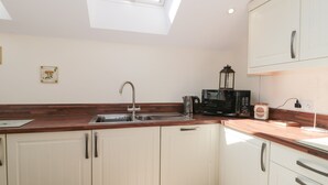 A modern kitchen with white cabinets, a wooden countertop, a skylight, a sink, a kettle, a microwave, and a coffee maker. - The Cider Shed (Winscombe)