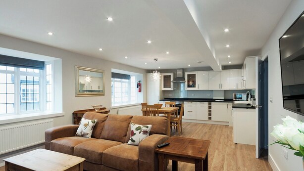 A modern living room with a brown sofa, wooden coffee table, and a dining area with a wooden table and chairs. - 2 bedroom accommodation in Duke Street (Duke Street)
