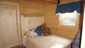 A wooden cabin bedroom with a single bed, a window with curtains, and a teddy bear on the bed. - Beautiful Mountain Cabin near Tetons Yellowstone (Dubois)