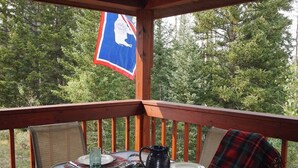 A covered outdoor dining area with a table set for two, surrounded by chairs, and a flag hanging above. - Beautiful Mountain Cabin near Tetons Yellowstone (Dubois)