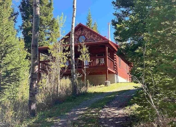 A log cabin with a porch, surrounded by trees.