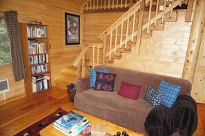 A wooden interior with a staircase, a sofa with patterned cushions, a bookshelf, and a coffee table with books. - Beautiful Mountain Cabin near Tetons Yellowstone (Dubois)