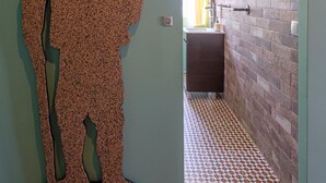 Un couloir orné d’une sculpture murale à motifs, doté d’un sol à motifs et comprenant une salle de bain avec un mur en briques et un luminaire suspendu.