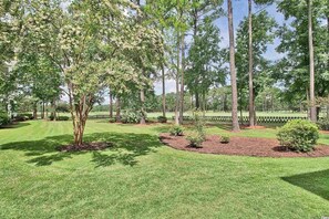 Surrounded by a variety of trees and shrubs, this peaceful outdoor space features a neatly trimmed lawn and a fenced area.