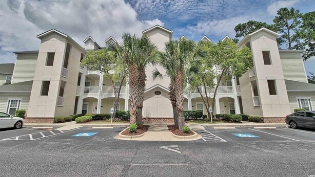 A multi-story hotel with a central courtyard, palm trees, and a parking lot with handicapped-accessible spaces. - New 2BR condo on 18th hole near beaches & ALL sports arenas—perfect getaway (Myrtle Beach)