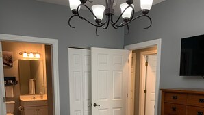 A bedroom with a patterned bedspread, a chandelier, a wooden dresser, and a television on the wall. - New 2BR condo on 18th hole near beaches & ALL sports arenas—perfect getaway (Myrtle Beach)