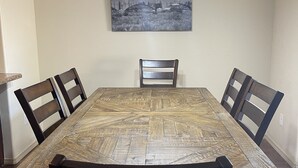 Un coin repas avec une grande table en bois, quatre chaises, un lustre et un tableau représentant un paysage urbain accroché au mur.