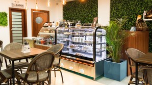 A bakery counter with pastries, a coffee machine, and a sign for bathrooms. - REEC Latacunga by Oro Verde Hotels (Latacunga)