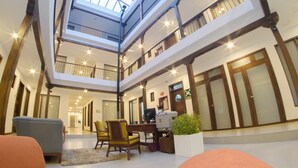A spacious atrium with a high ceiling and a skylight, featuring a central seating area with chairs and a desk, surrounded by wooden-framed windows and doors. - REEC Latacunga by Oro Verde Hotels (Latacunga)