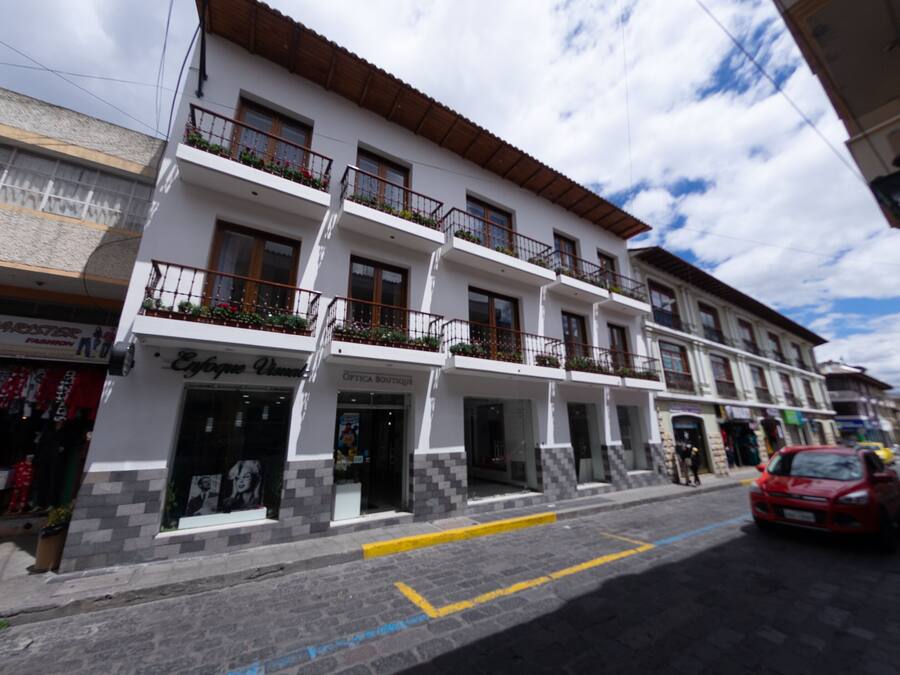 Un edificio de varios pisos con balcones, tiendas y una calle adoquinada.