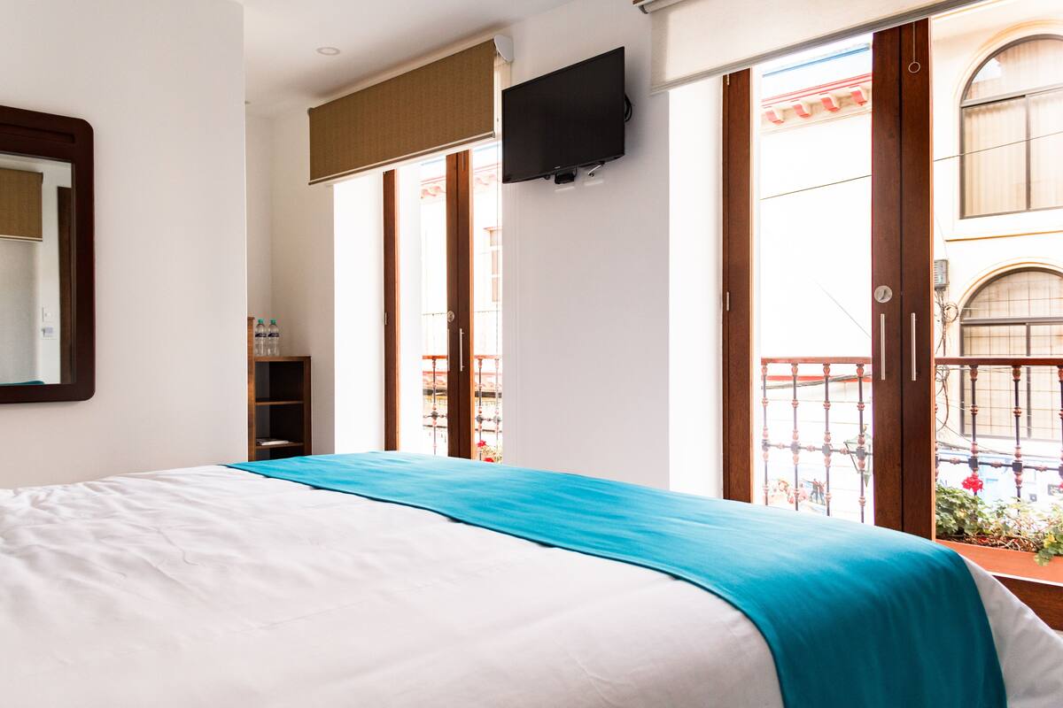 Une chambre d’hôtel avec un lit, un téléviseur fixé au mur et un balcon donnant sur la rue.