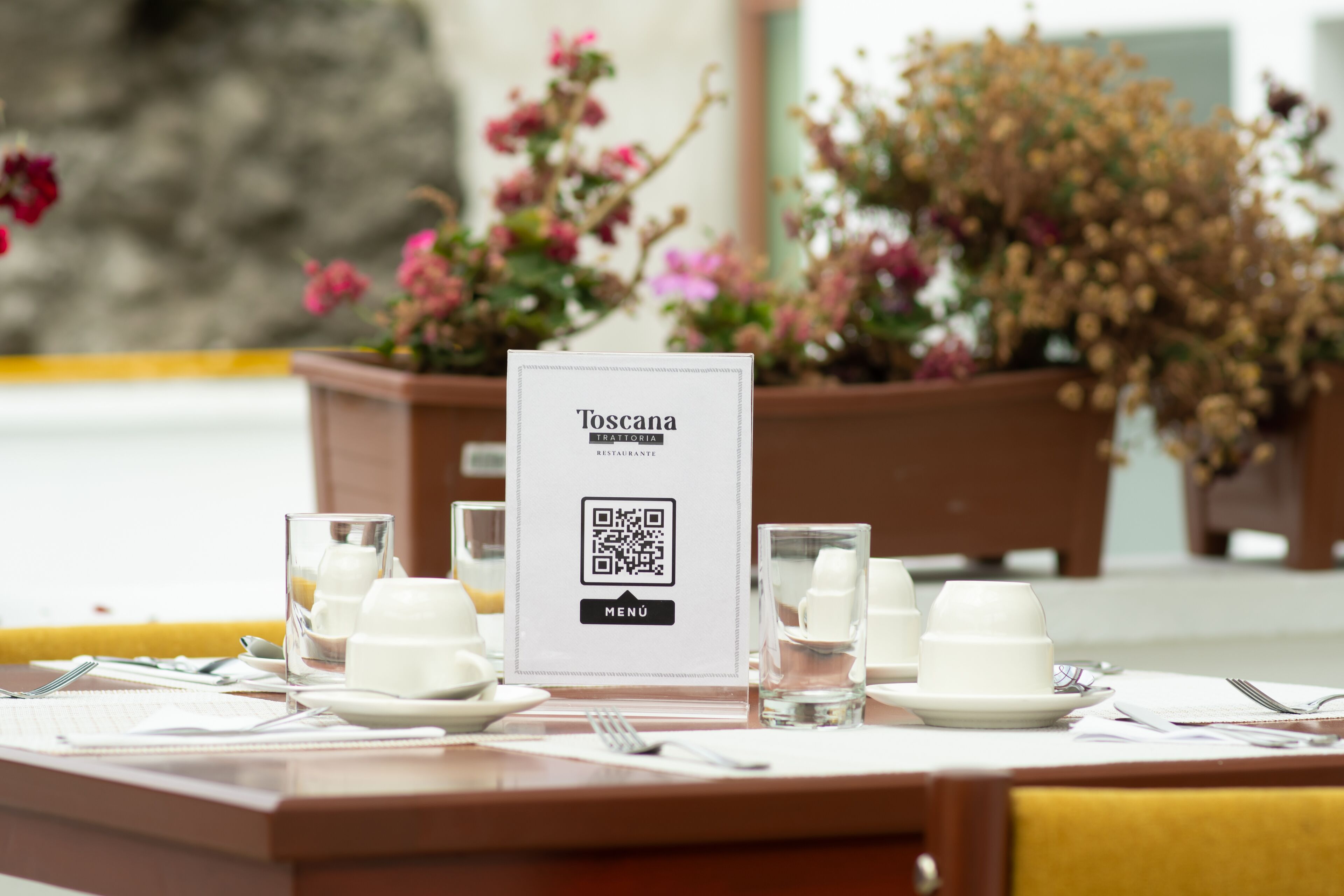 A table set with white dishes, glasses, and cutlery, with a QR code menu sign in the center.