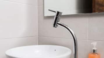Un baño con un lavamanos blanco, grifo cromado y un espejo encima.